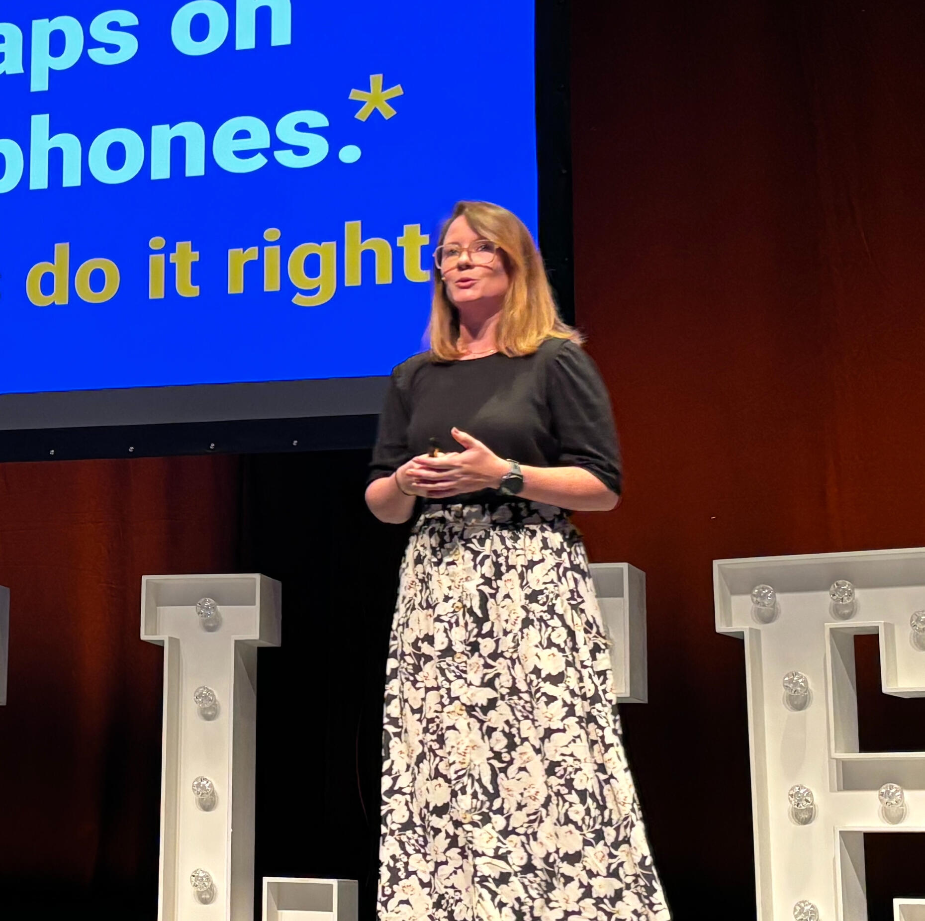 Photo of Robin giving a presentation pointing to a slide with code, with a microphone in her hand
